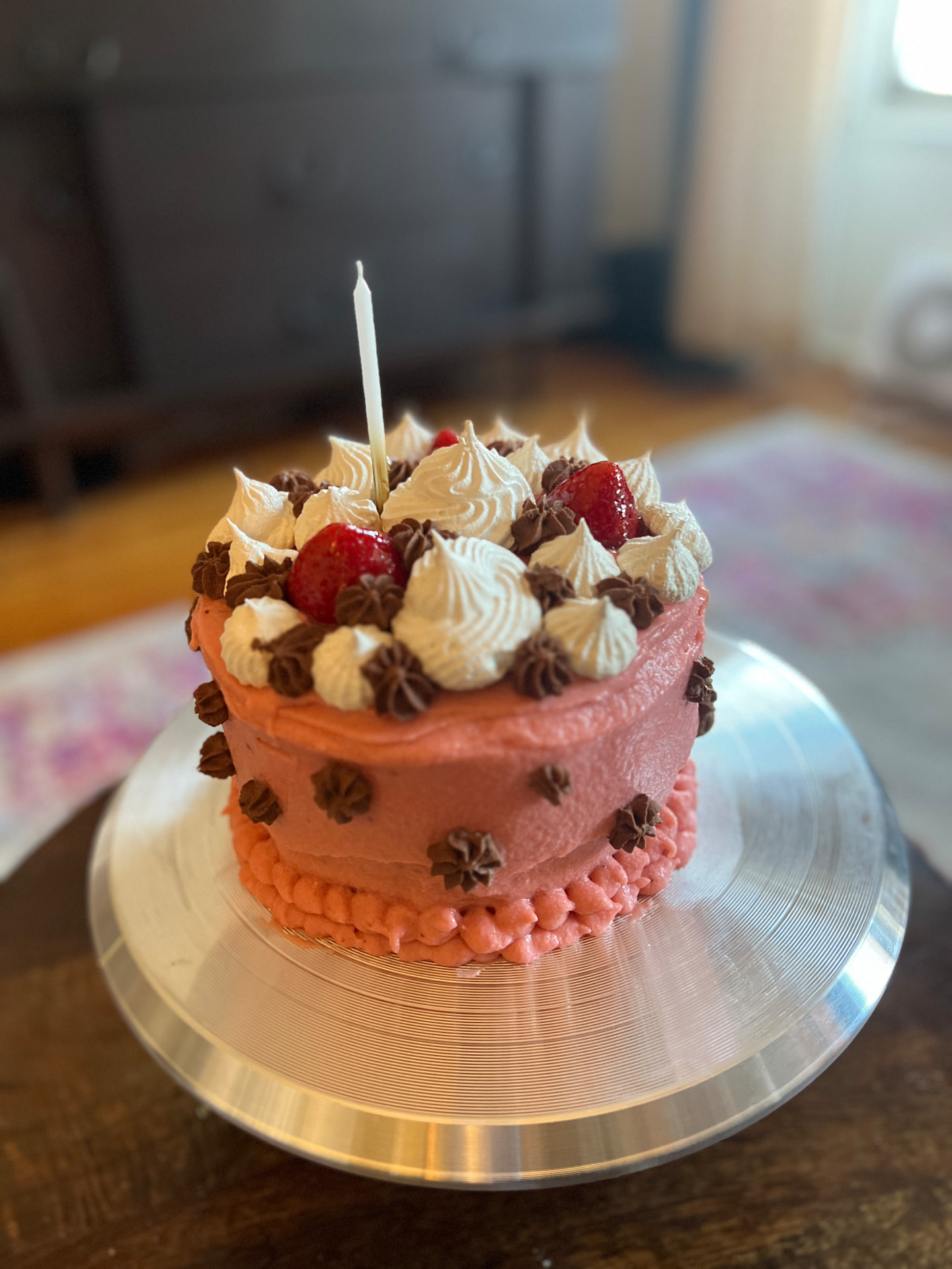 A small pink buttercream birthday cake with a single candle, piped cream and chocolate stars and strawberries