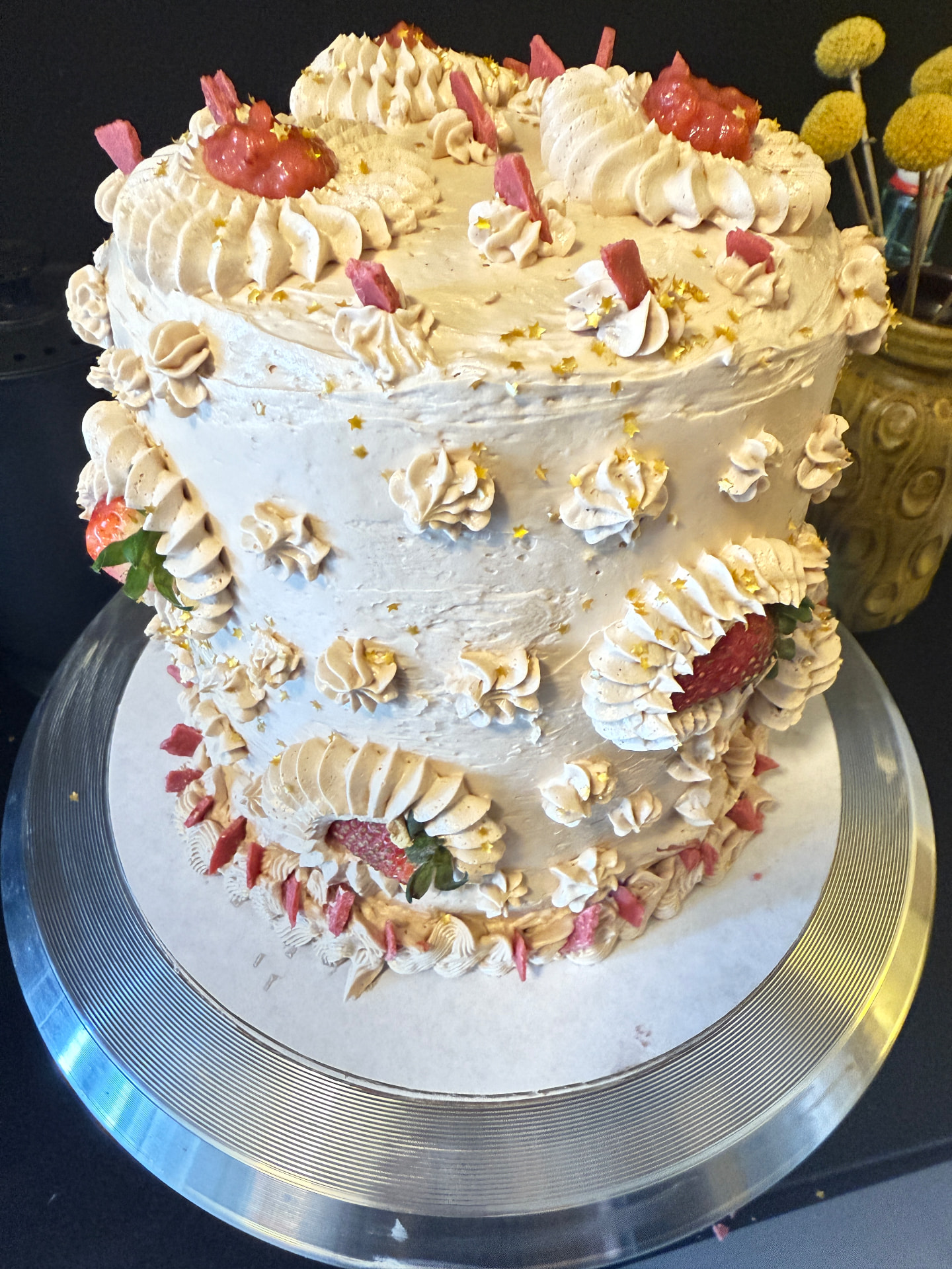 A tall vanilla bean buttercream cake piped with rosettes, strawberry pieces and gold stars
