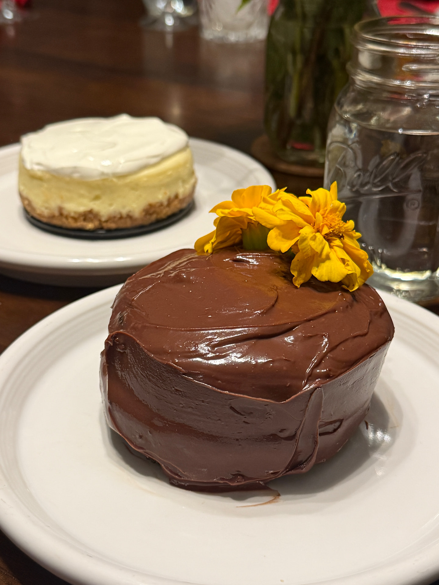 A glossy chocolate ganache cake on a white plate, finished with marigold blossoms