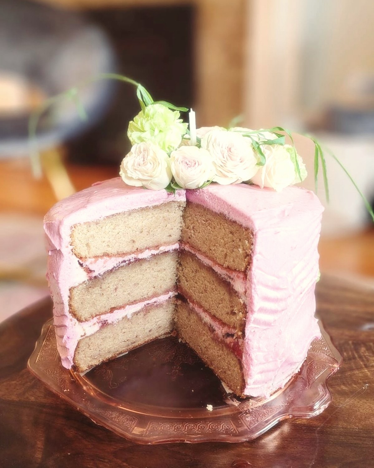 A three-layer pink buttercream cake topped with garden roses, cut to show the layers
