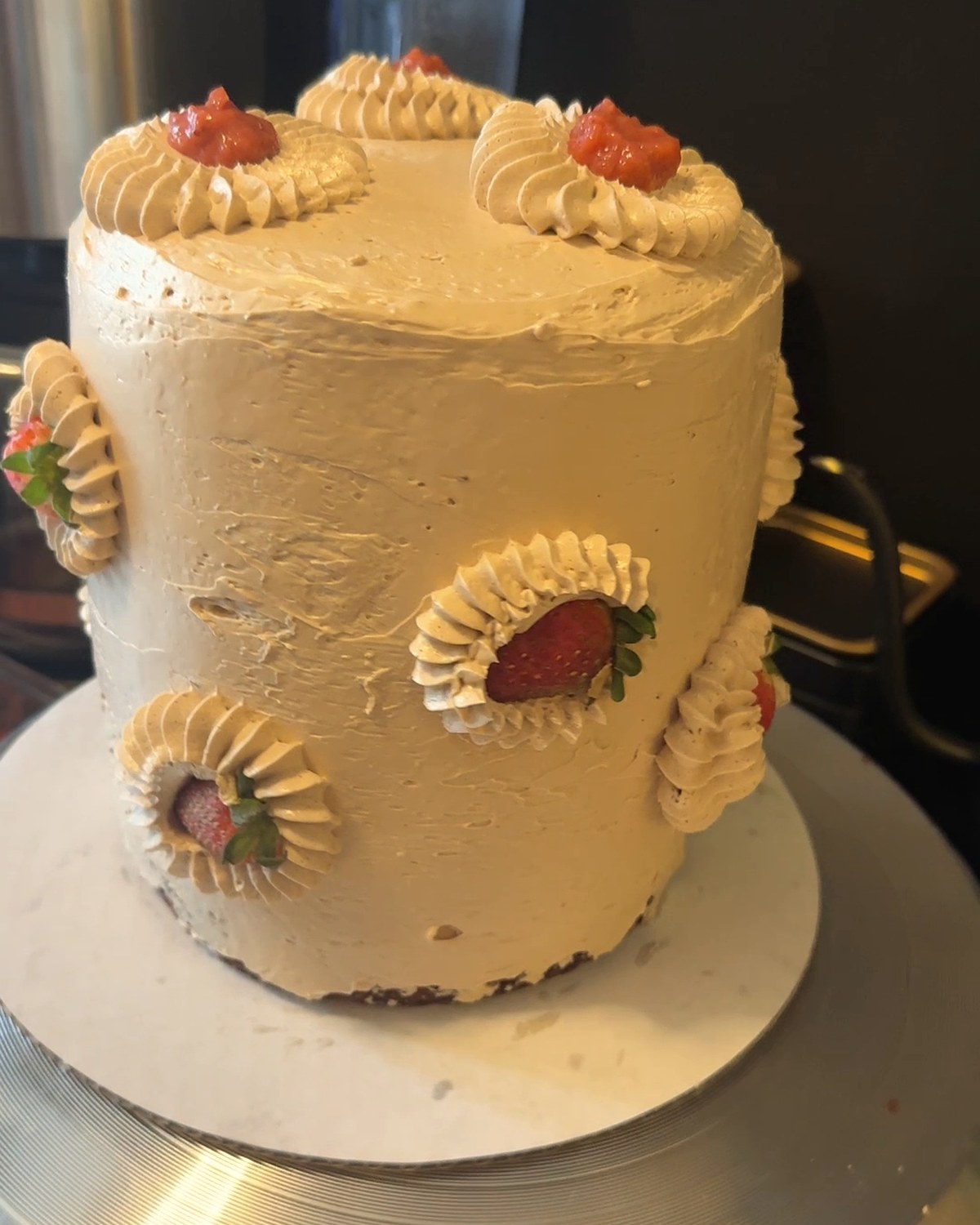 A tall buttercream cake turning on the stand, piped rosettes cradling fresh strawberries